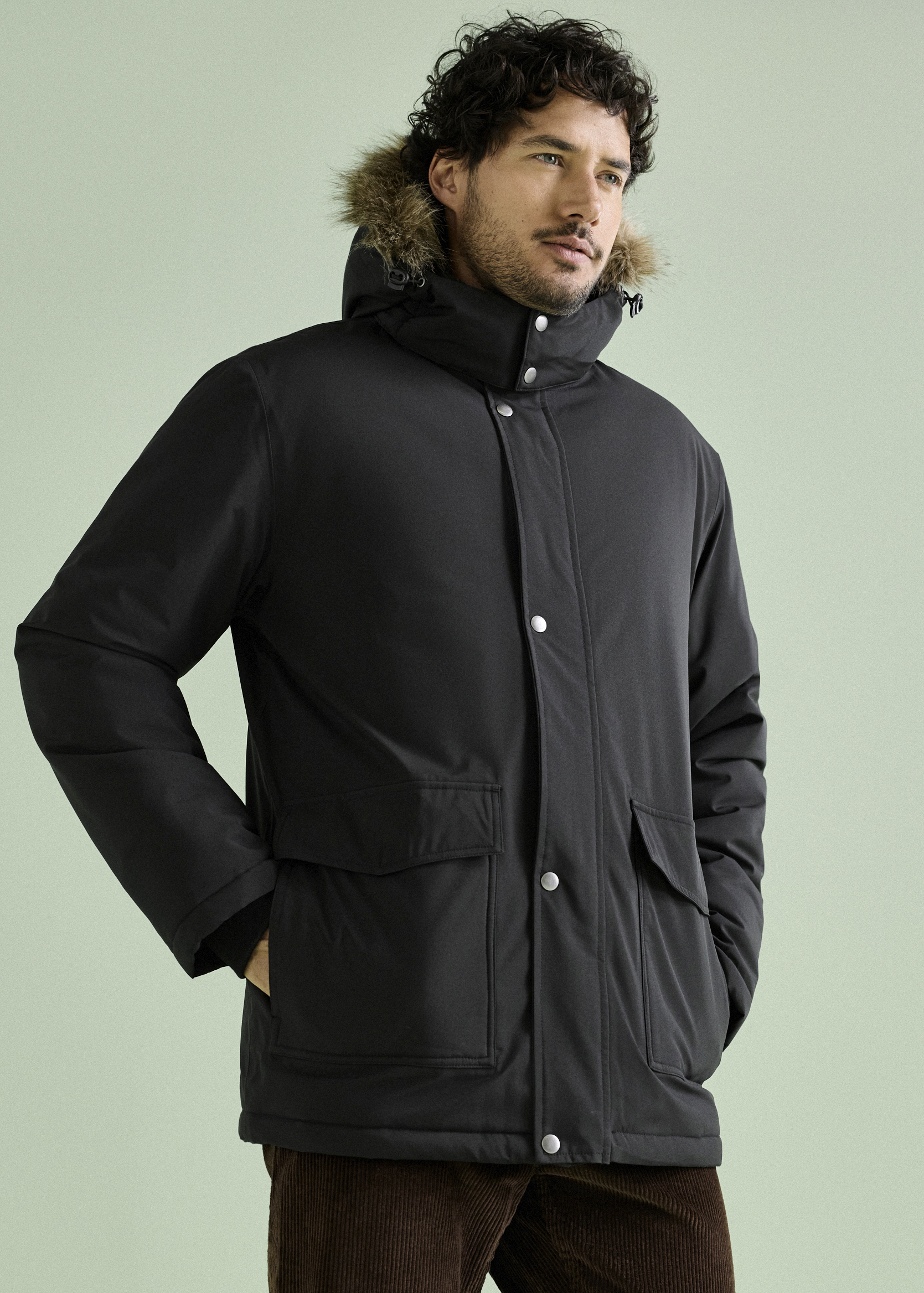 Mann trägt einen schwarzen Parka mit Fellkapuze und braune Cordhose.
