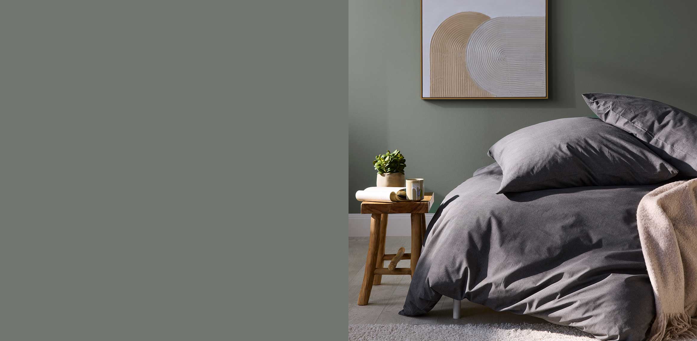 Elegante graue Bettwäsche harmoniert mit grüner Wand. Eine Pflanze ergänzt das schlichte Schlafzimmerambiente.
