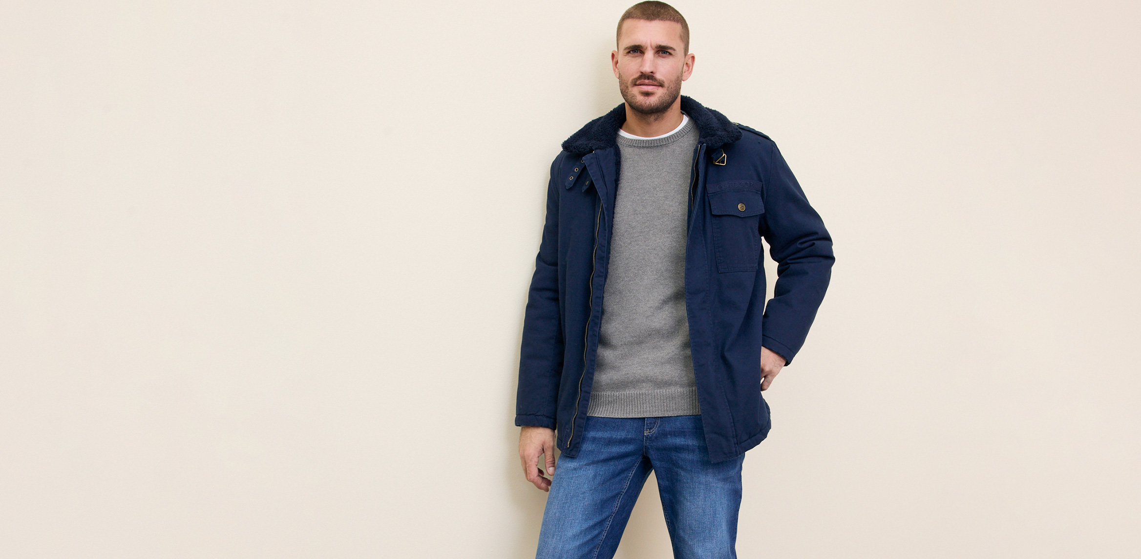 Dunkelblaue Jacke über grauem Pullover, kombiniert mit blauen Jeans.