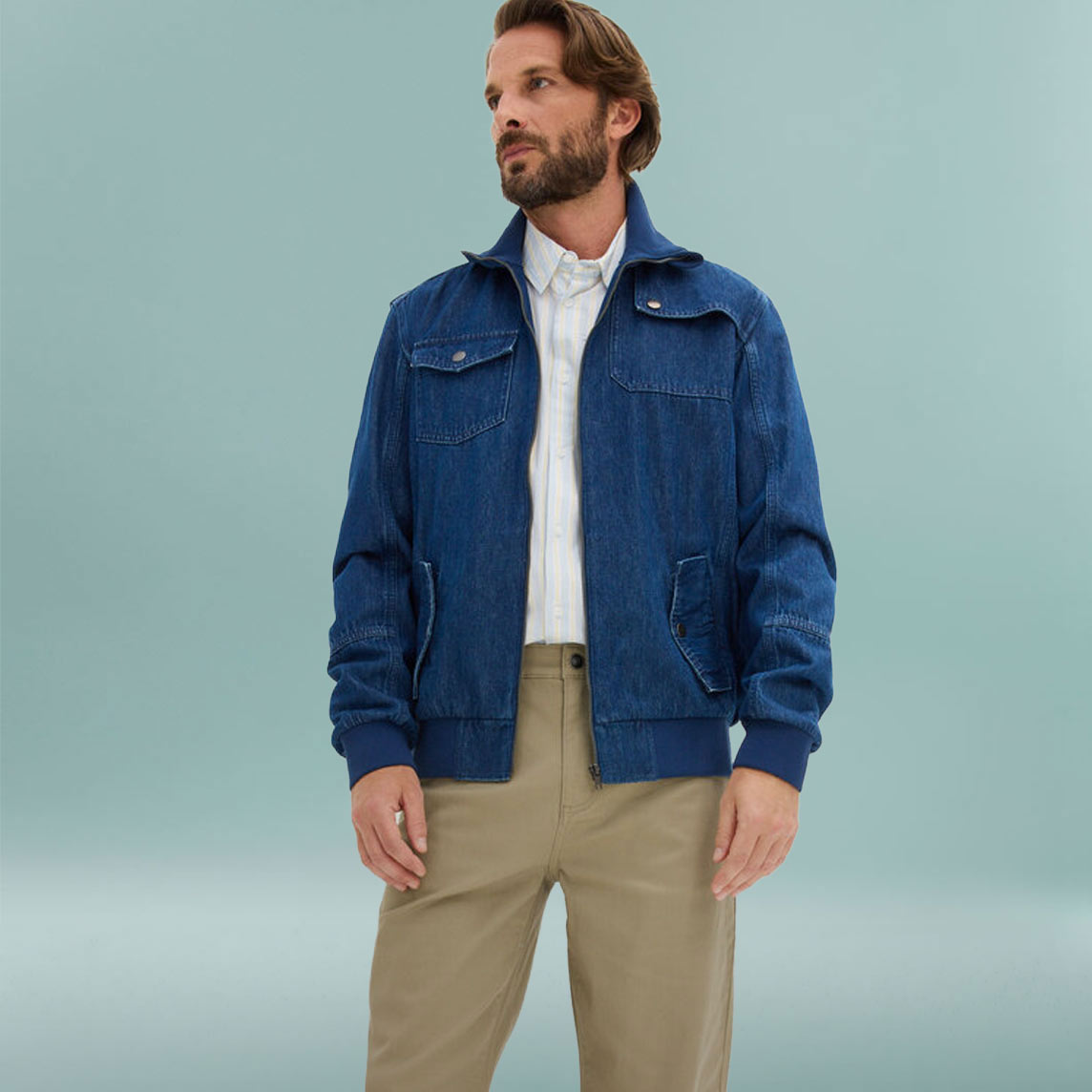 Mann trägt blaue Jeansjacke über weißem Shirt und beige Hose.