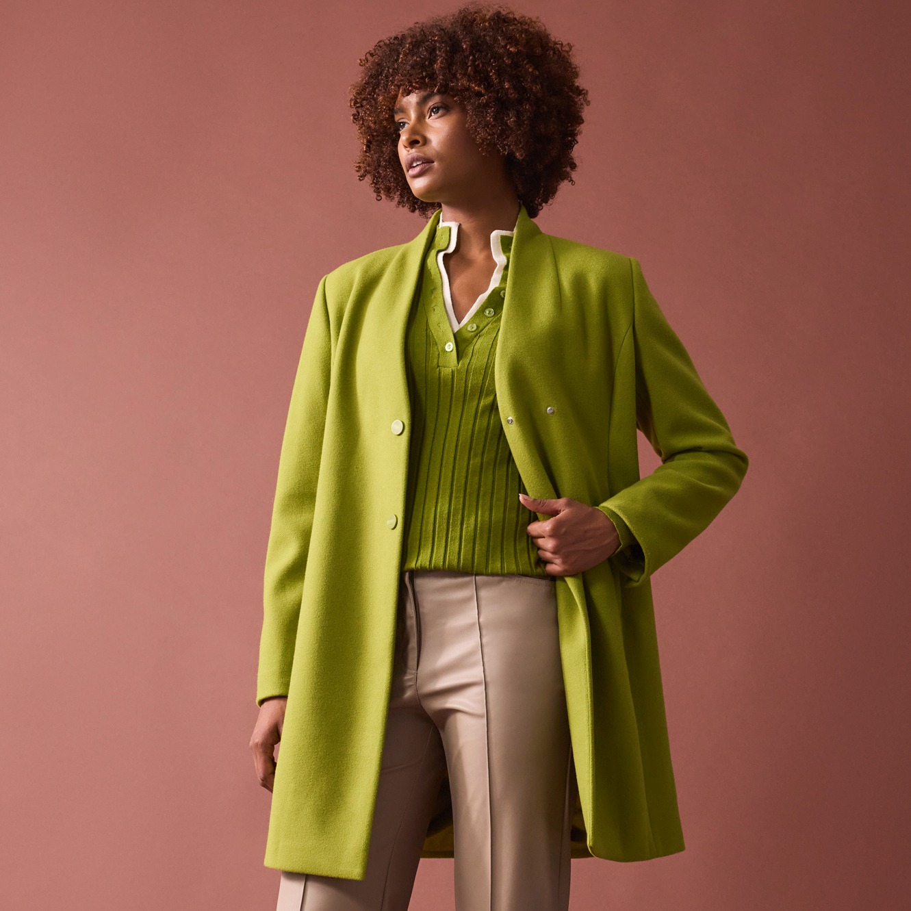 Grüner Mantel und Pullover, kontrastiert mit beiger Hose.