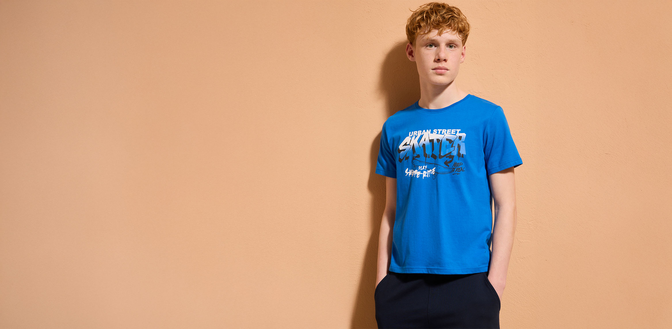 Blaues T-Shirt mit aufgedrucktem Schriftzug, dunkle Hose. Lässiger Stil für den Alltag.