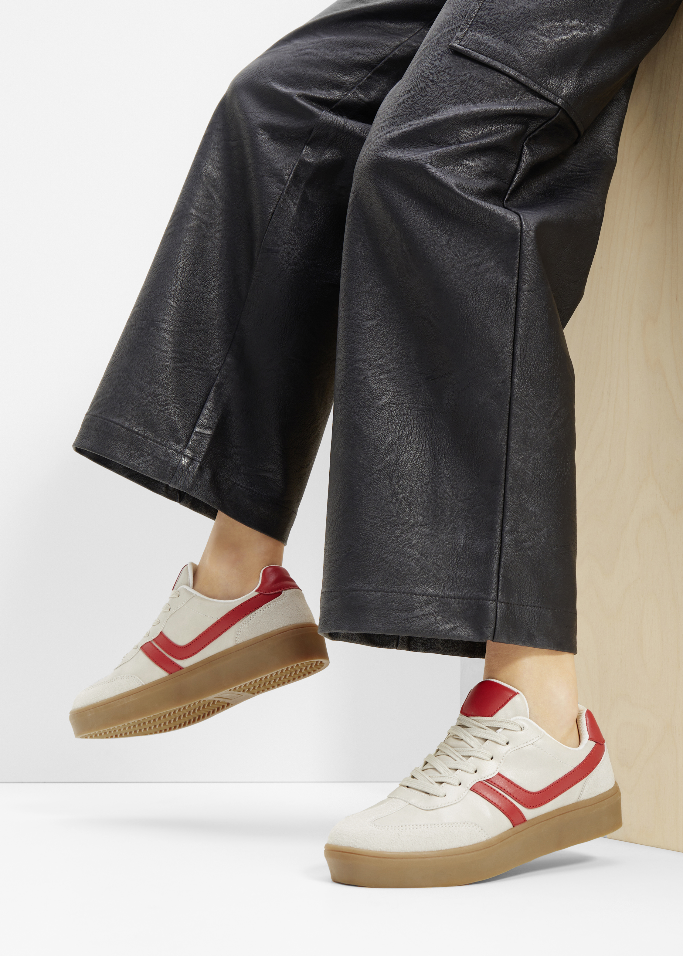 Schwarze Lederhose kombiniert mit weißen Sneakern mit roten Details und Gummisohle.