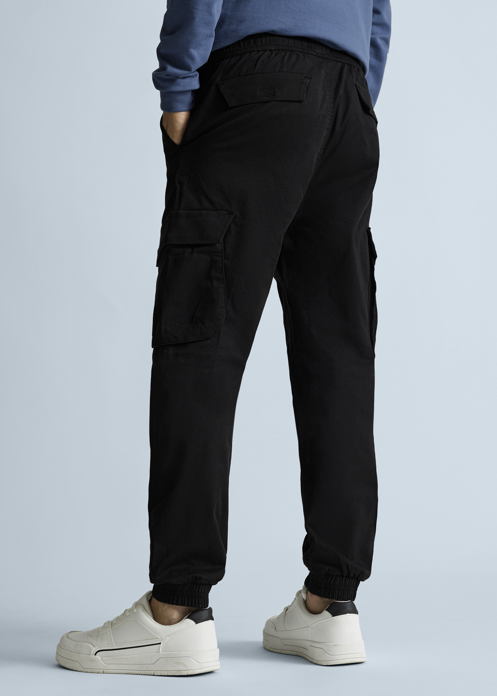 Lässige schwarze Cargohose mit Bündchen, kombiniert mit blauem Pullover und hellen Sneakern.