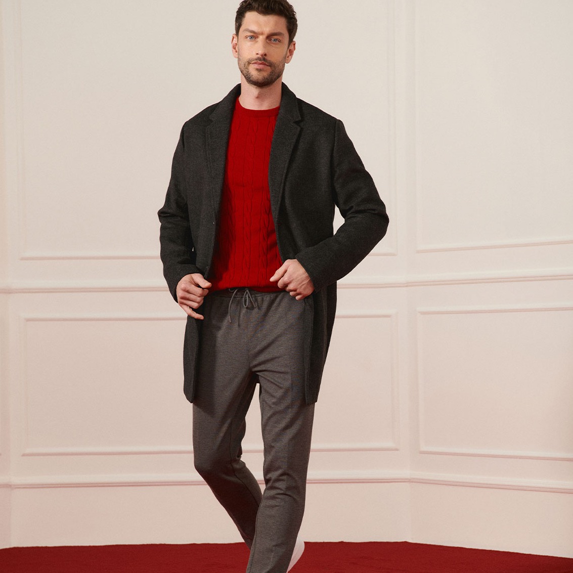 Dunkler Wollmantel, roter Pullover und graue Hose für einen stilvollen Look.