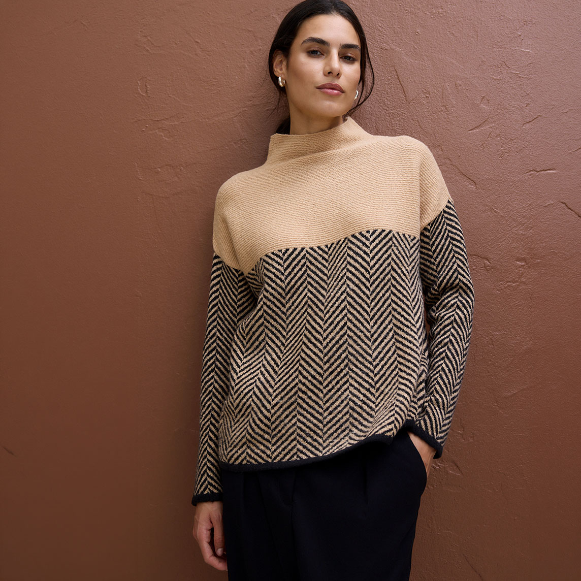 Stylisher Pullover: beiger Rollkragen, schwarz-beiges Fischgrätmuster und elegante schwarze Hose.