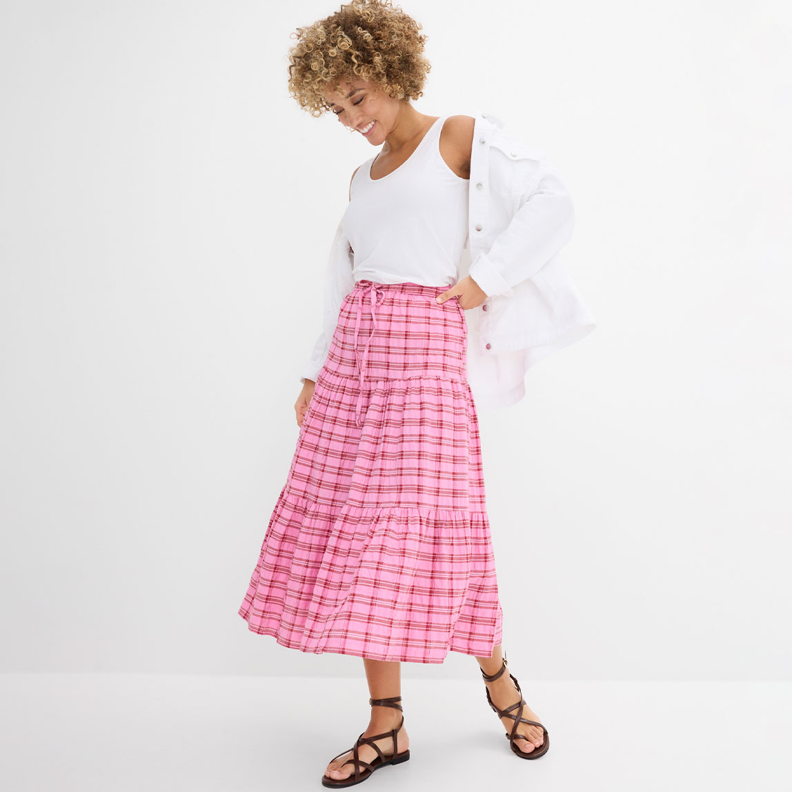 Weißes schulterfreies Oberteil kombiniert mit einem rosa-weiß karierten langen Rock und schwarzen Sandalen.