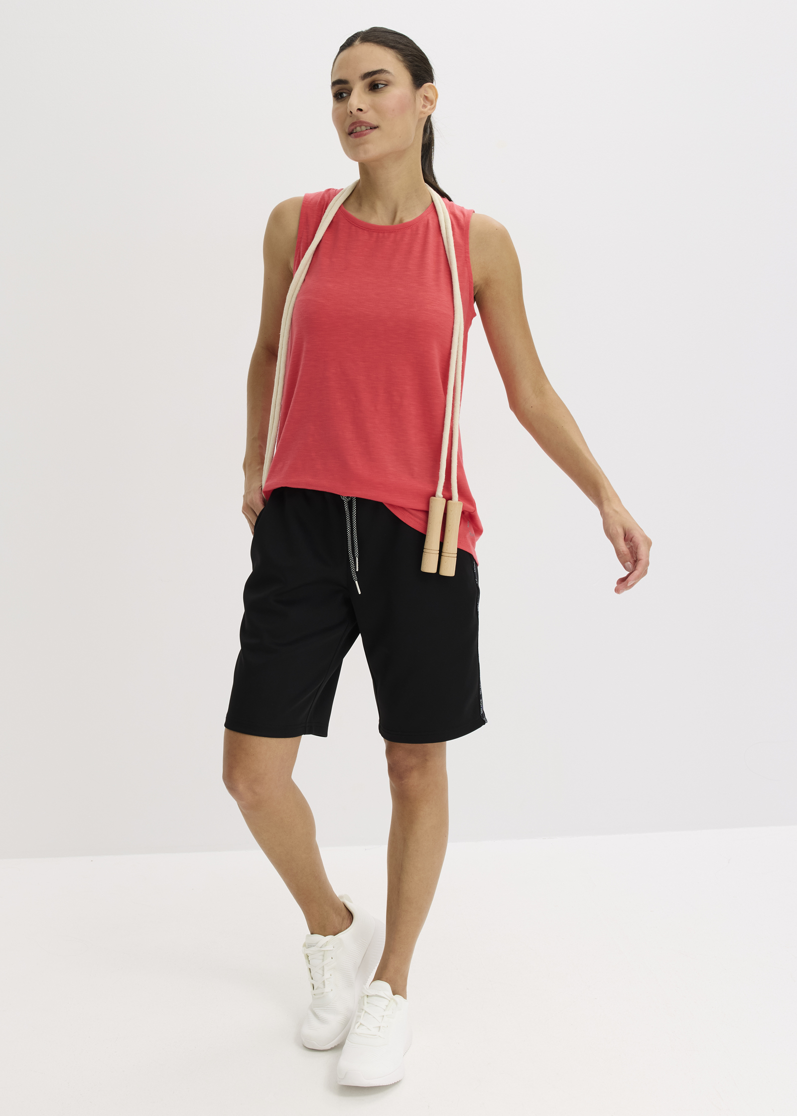 Rotes Tanktop, schwarze Shorts und weiße Sneaker bilden das sportliche Outfit.