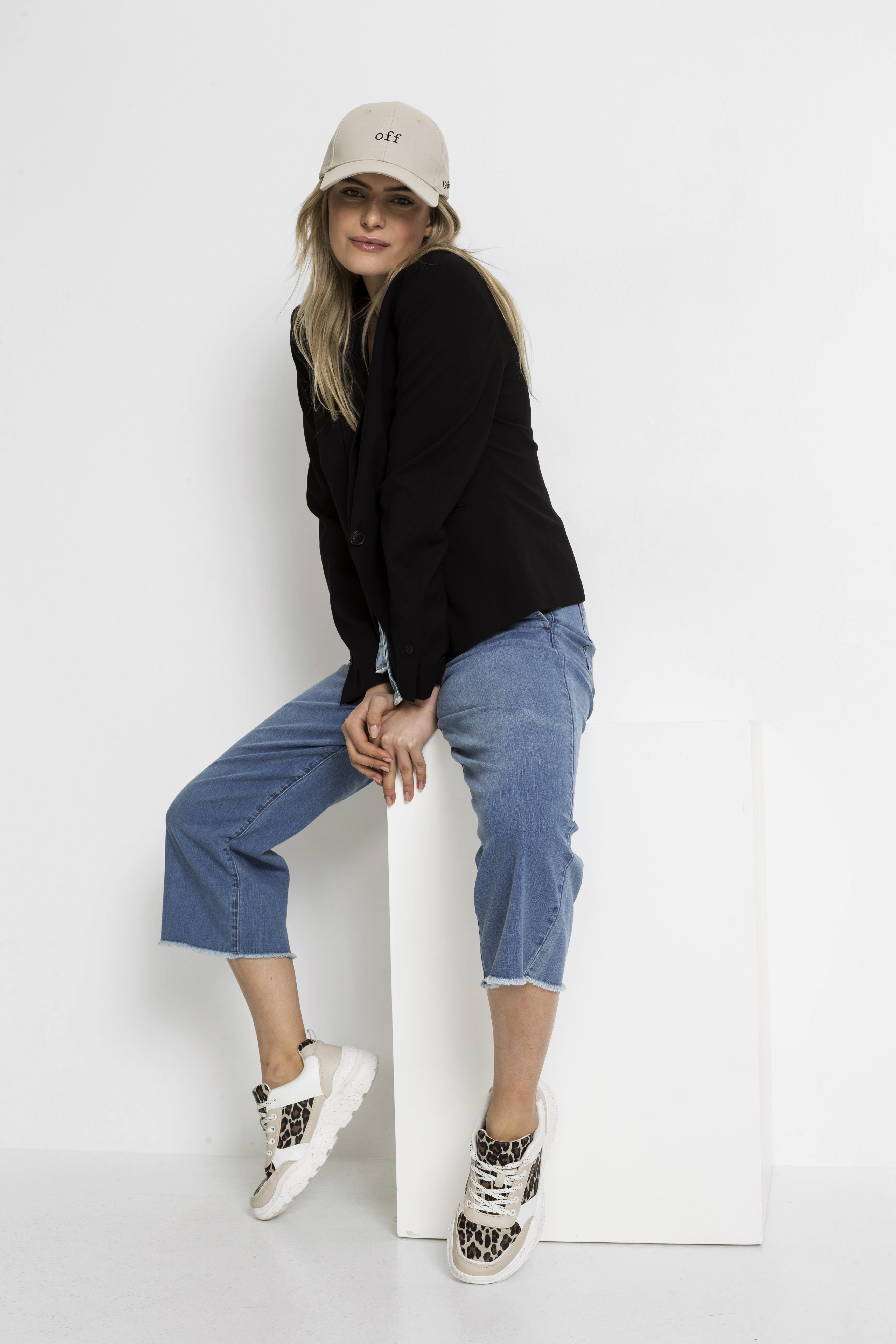 Lässiger Look: Beiger Hut, schwarzer Pullover, Jeans-Capris und stylische Sneaker mit Leopardenmuster.