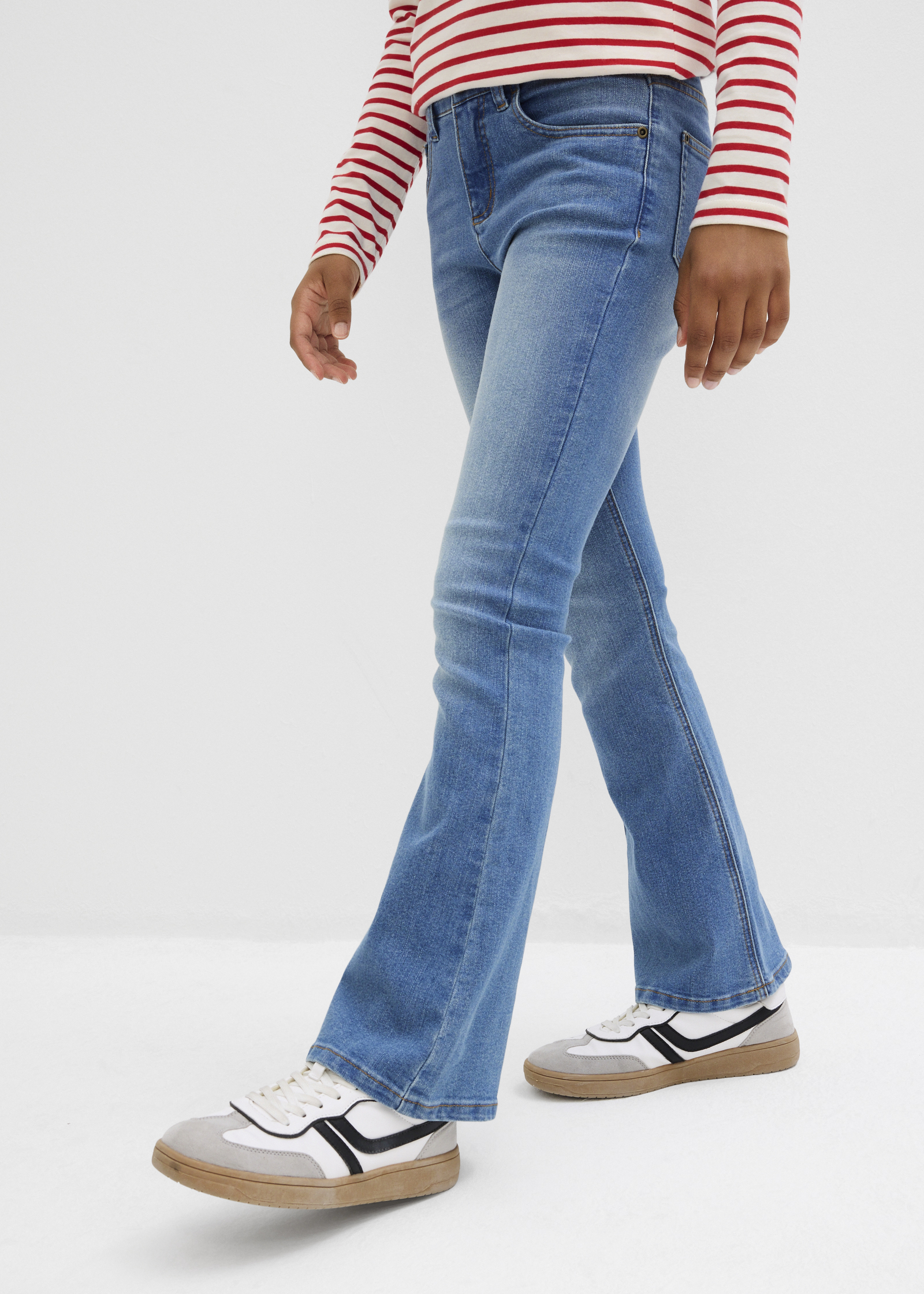 Das Kind trägt gestreiftes Langarmshirt, blaue Schlagjeans und weiße Sneaker.