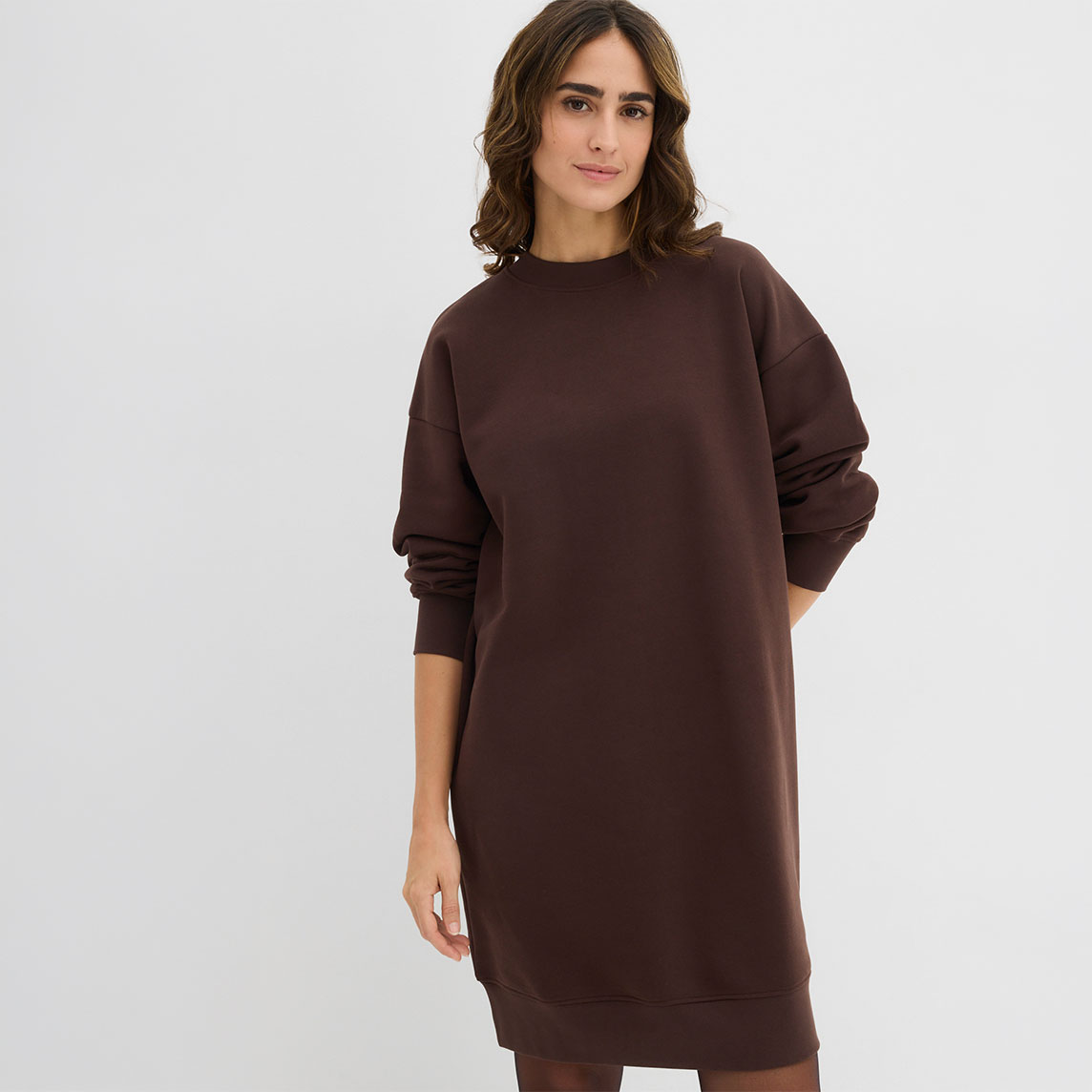 Eine Frau trägt ein langes, locker sitzendes, dunkelbraunes Sweatshirt-Kleid.