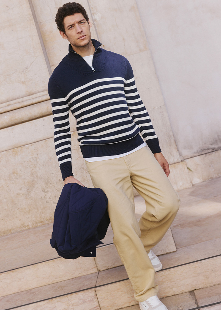 Gestreifter Pullover in Marineblau und Weiß, beige Hose und dunkelblaue Jacke.