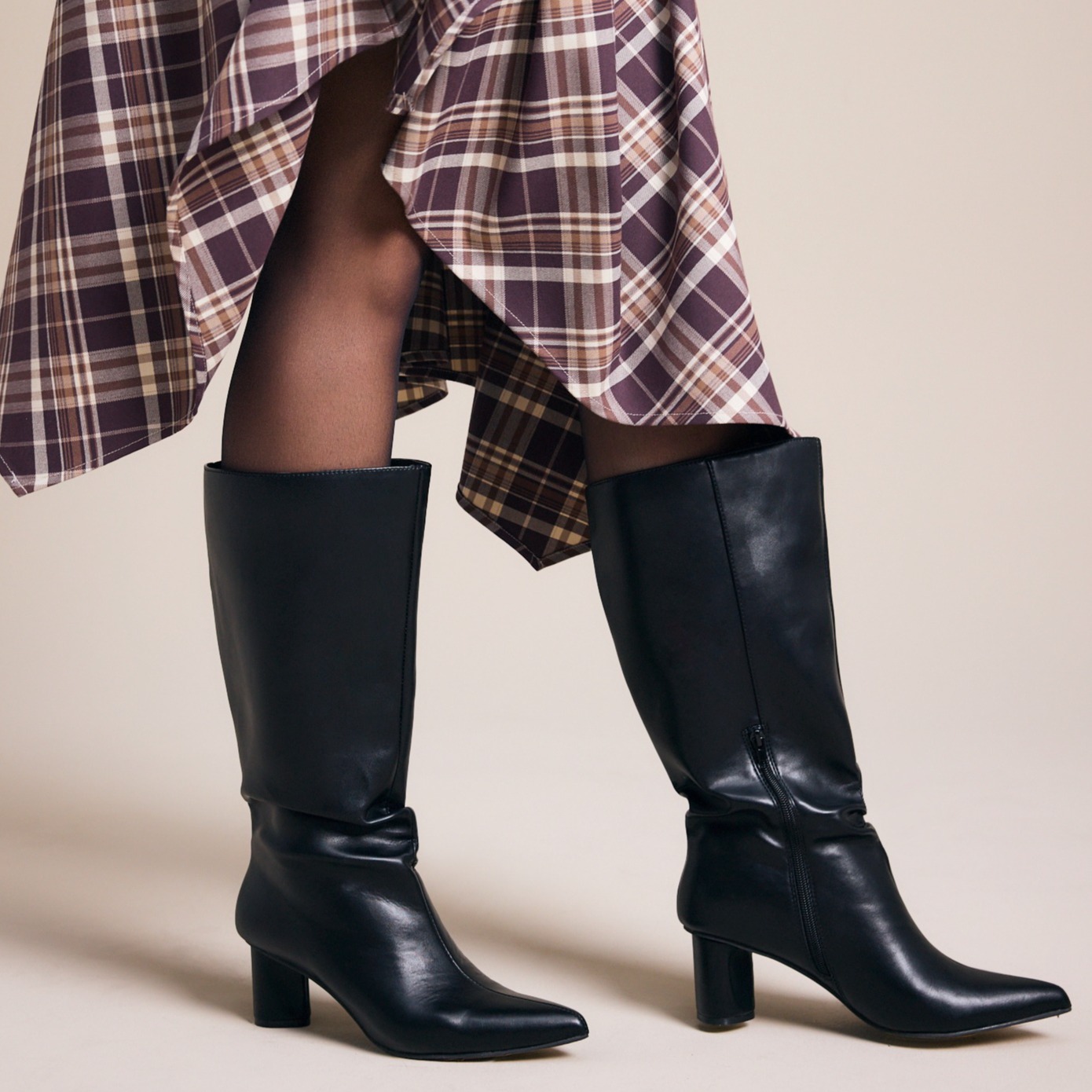 Modischer Auftritt: Karierter Rock, schwarze Strumpfhose und elegante schwarze Stiefel.