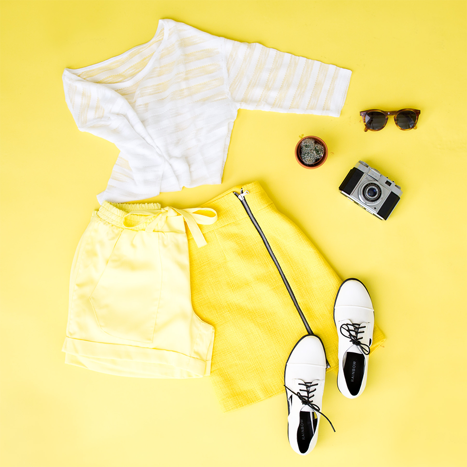 Sommerliches Outfit: Weißes T-Shirt, gelbe Shorts, weiße Sneakers. Accessoires: Sonnenbrille, Kamera und Kompass.