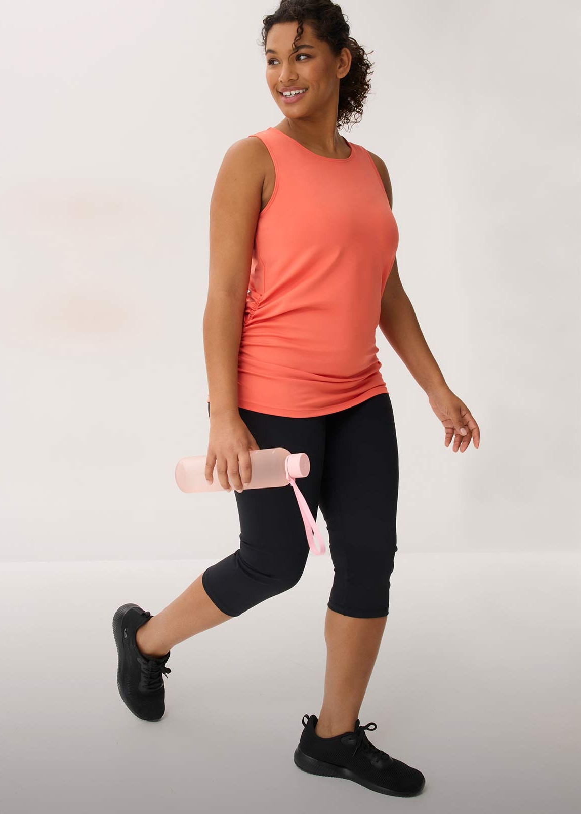 Sportliches Outfit mit korallenfarbenem Tanktop und schwarzer Caprihose.