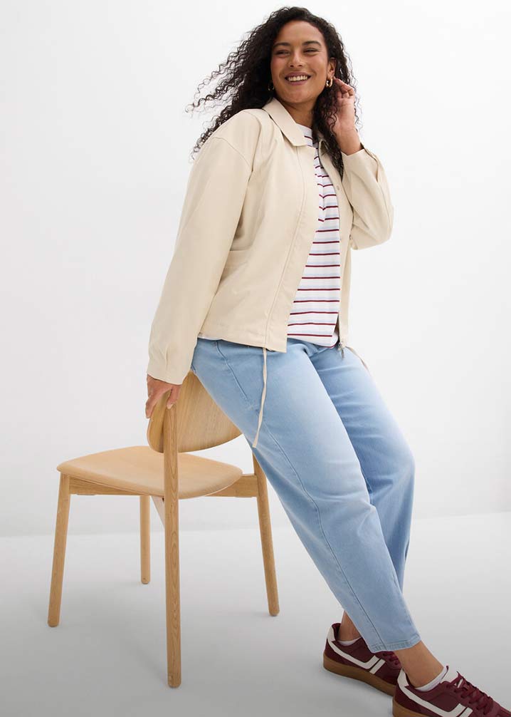 Cremefarbene Jacke über gestreiftem Shirt, hellblaue Jeans und braune Schuhe. 