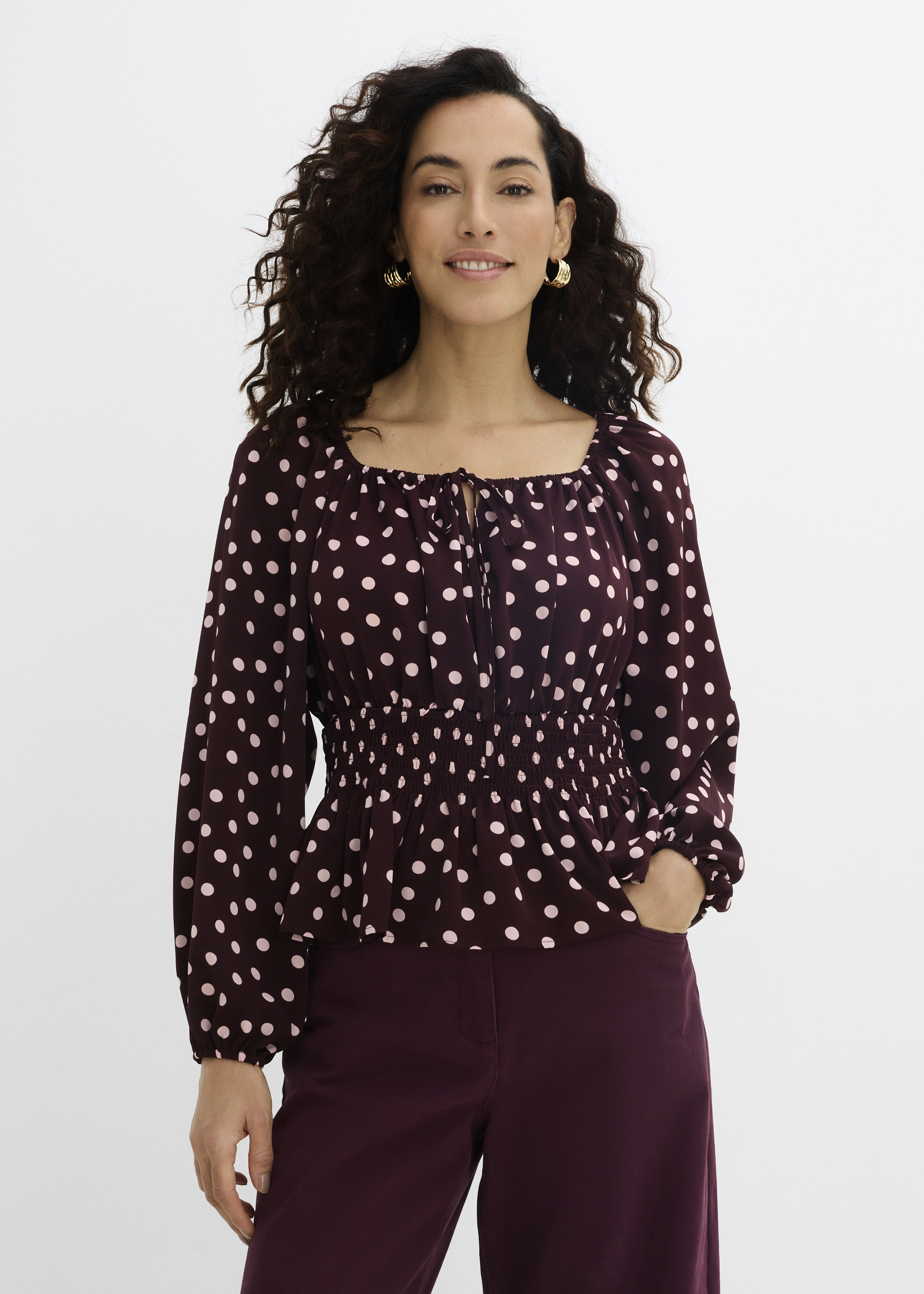 Weinrote Polka-Dot-Bluse mit gesmoktem Bund und passender Hose, dazu goldene Ohrringe.