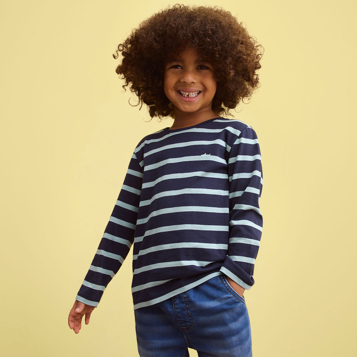 Ein kleiner Junge trägt ein blau-weiß gestreiftes Langarmshirt und eine blaue Jeans.