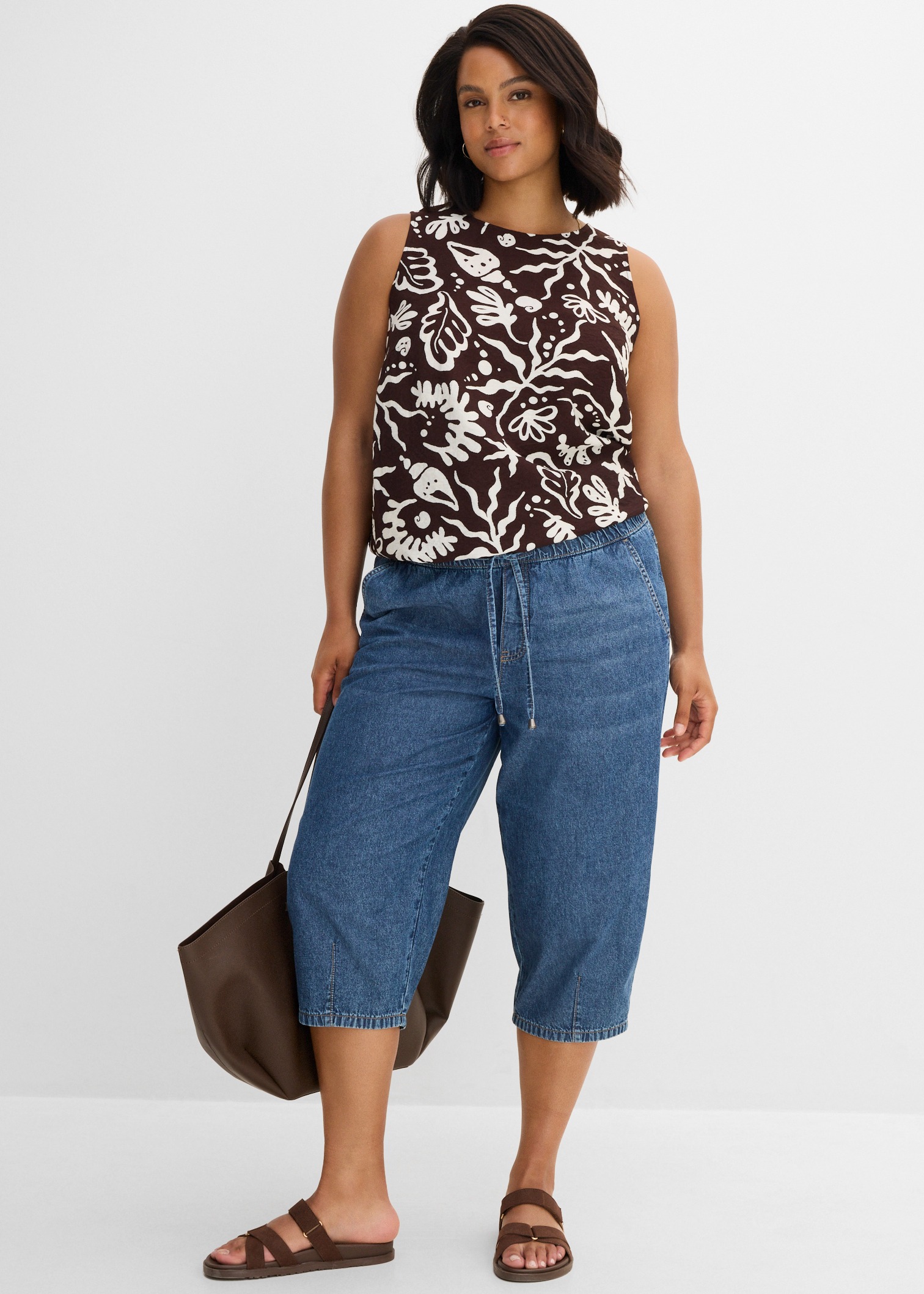 Gemustertes Top,  Denim-Caprihose, braune Sandalen und Shopper. 