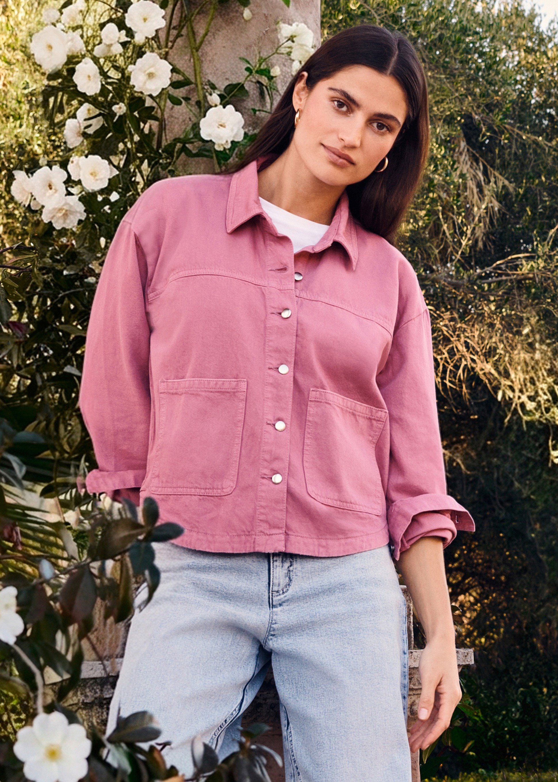 Rosa Jacke mit großen Taschen über weißem Shirt, kombiniert mit heller Jeans.