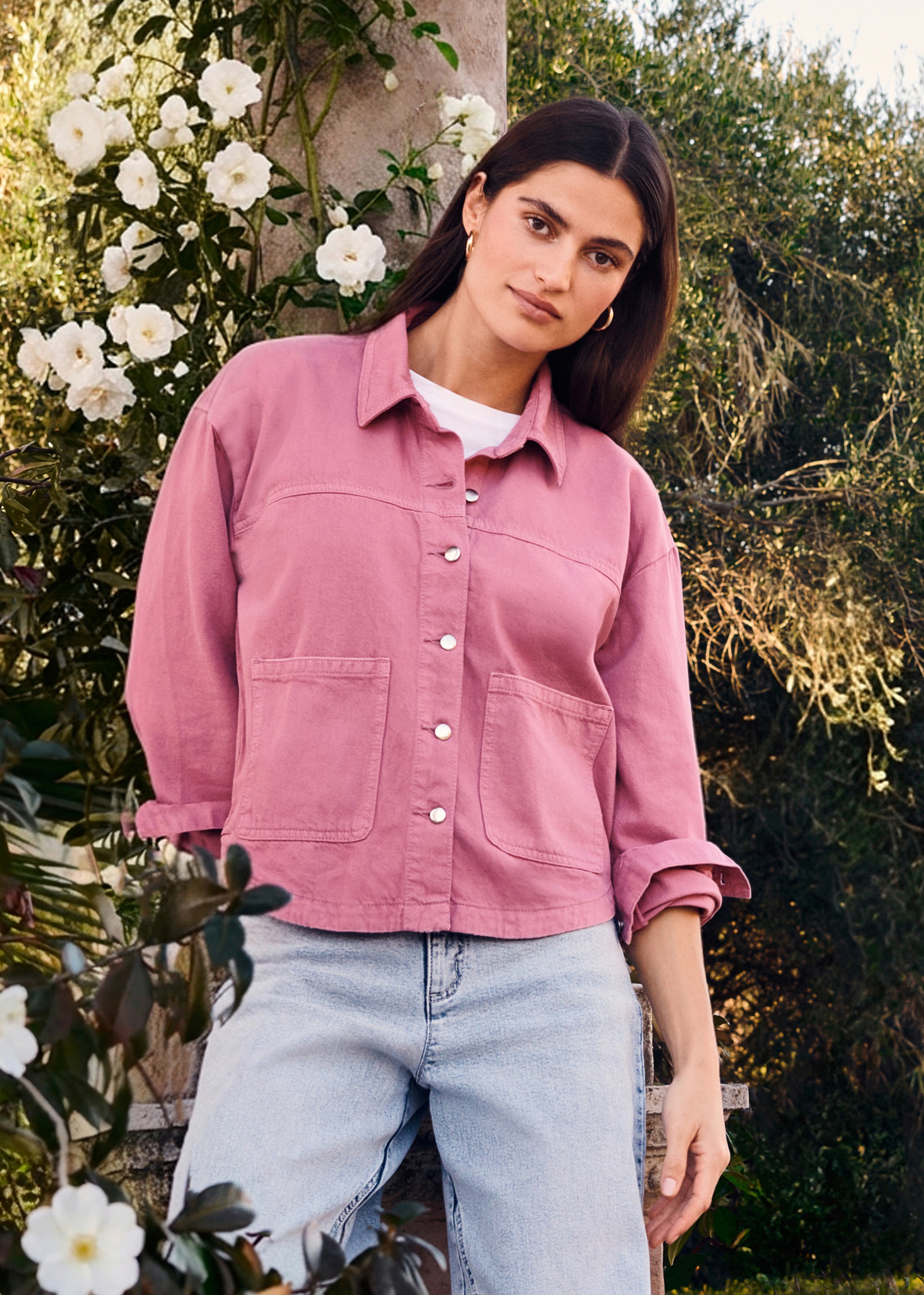 Rosa Jacke mit großen Taschen über weißem Shirt, kombiniert mit heller Jeans.