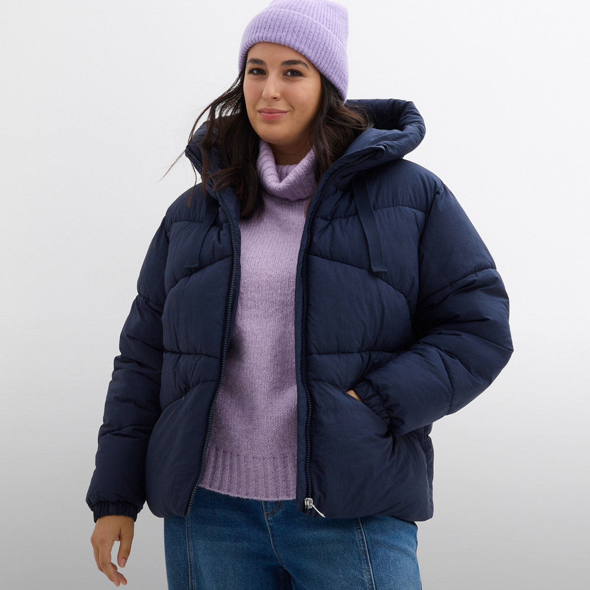 Dunkelblaue Daunenjacke, lila Rollkragen und Strickmütze.