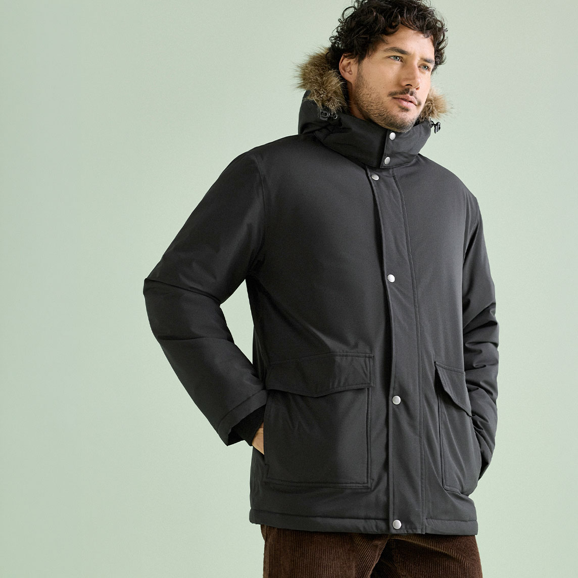 Ein Mann trägt einen robusten schwarzen Parka mit Fellkapuze und braune Cordhose.