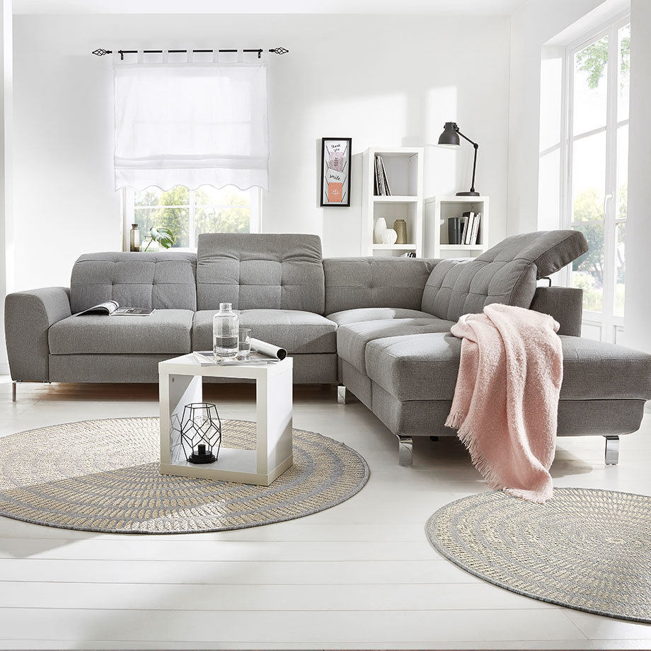 Graues Ecksofa mit weichen Kissen, rosa Decke verleiht dem Raum einen warmen Akzent.