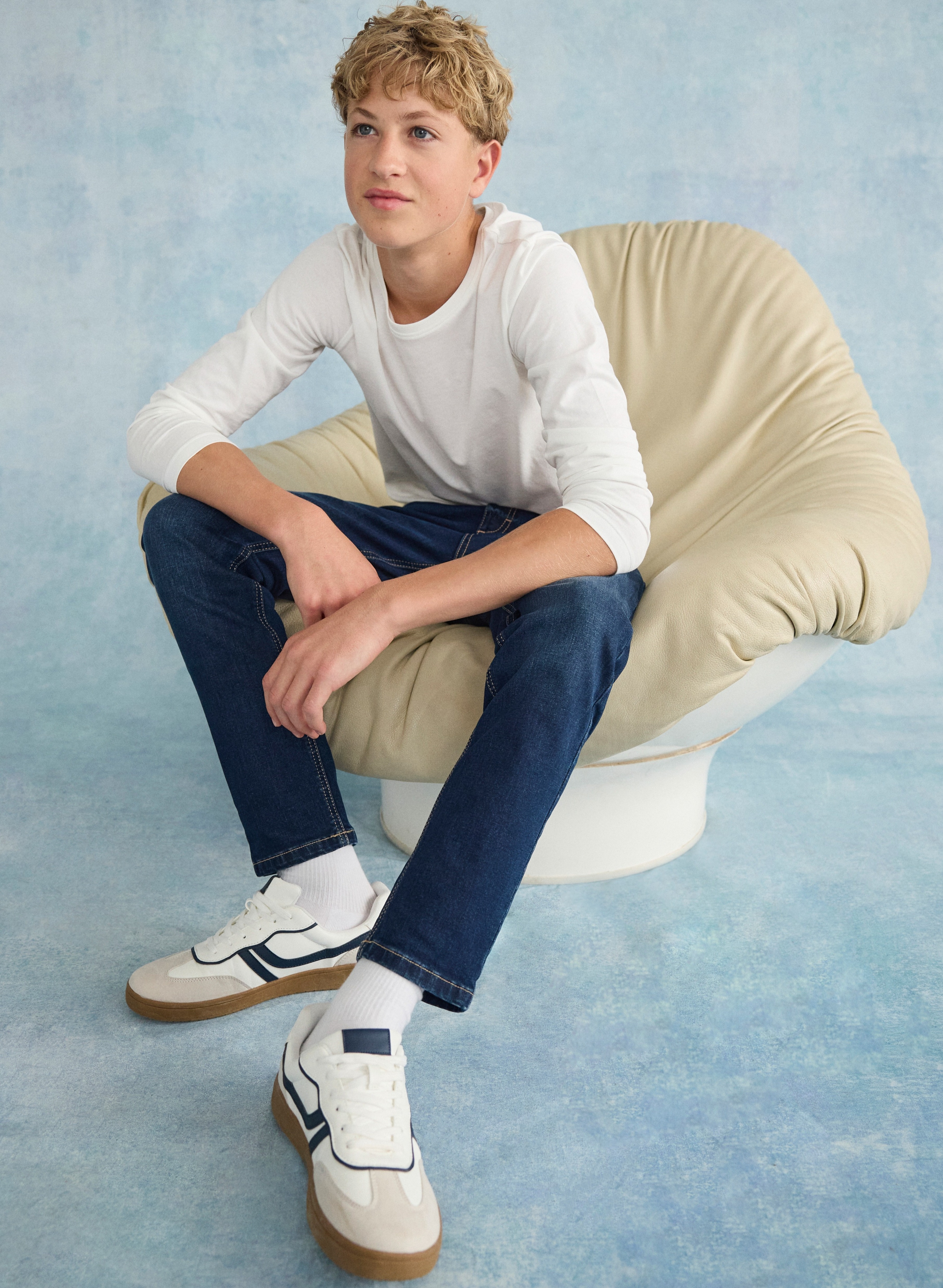 Weißes Langarmshirt, blaue Jeans und weiße Sneaker mit dunklen Akzenten.