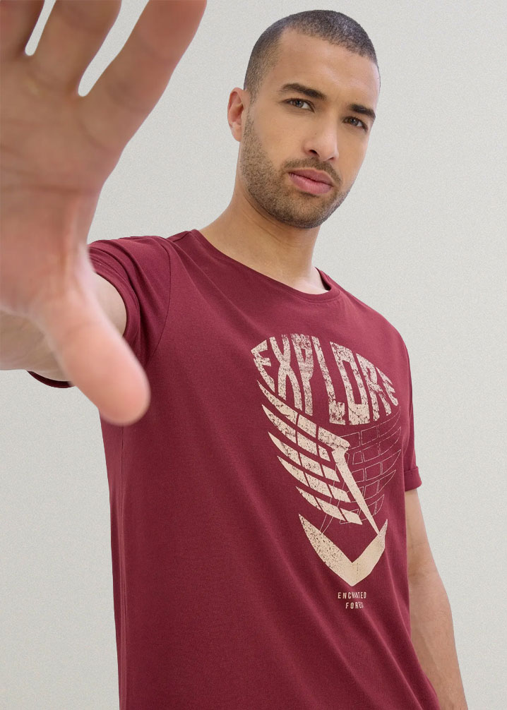 Der Mann trägt ein bordeauxrotes T-Shirt mit einem auffälligen 'EXPLORE'-Druck.