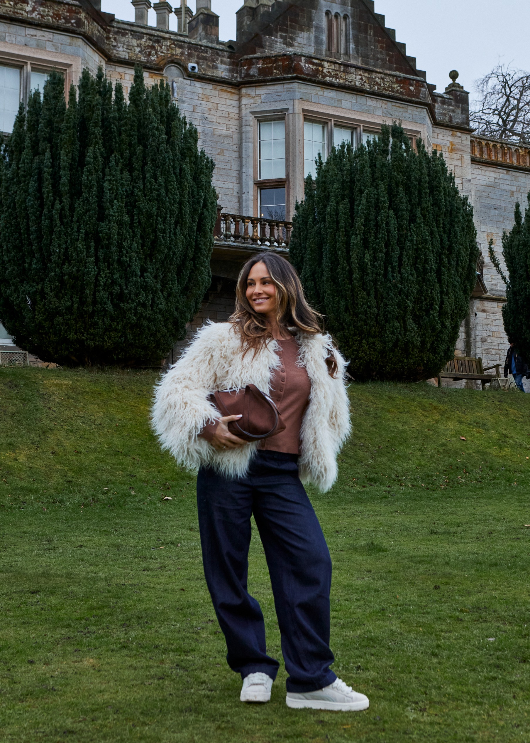 Flauschige weiße Jacke, brauner Pullover und weite Jeans.