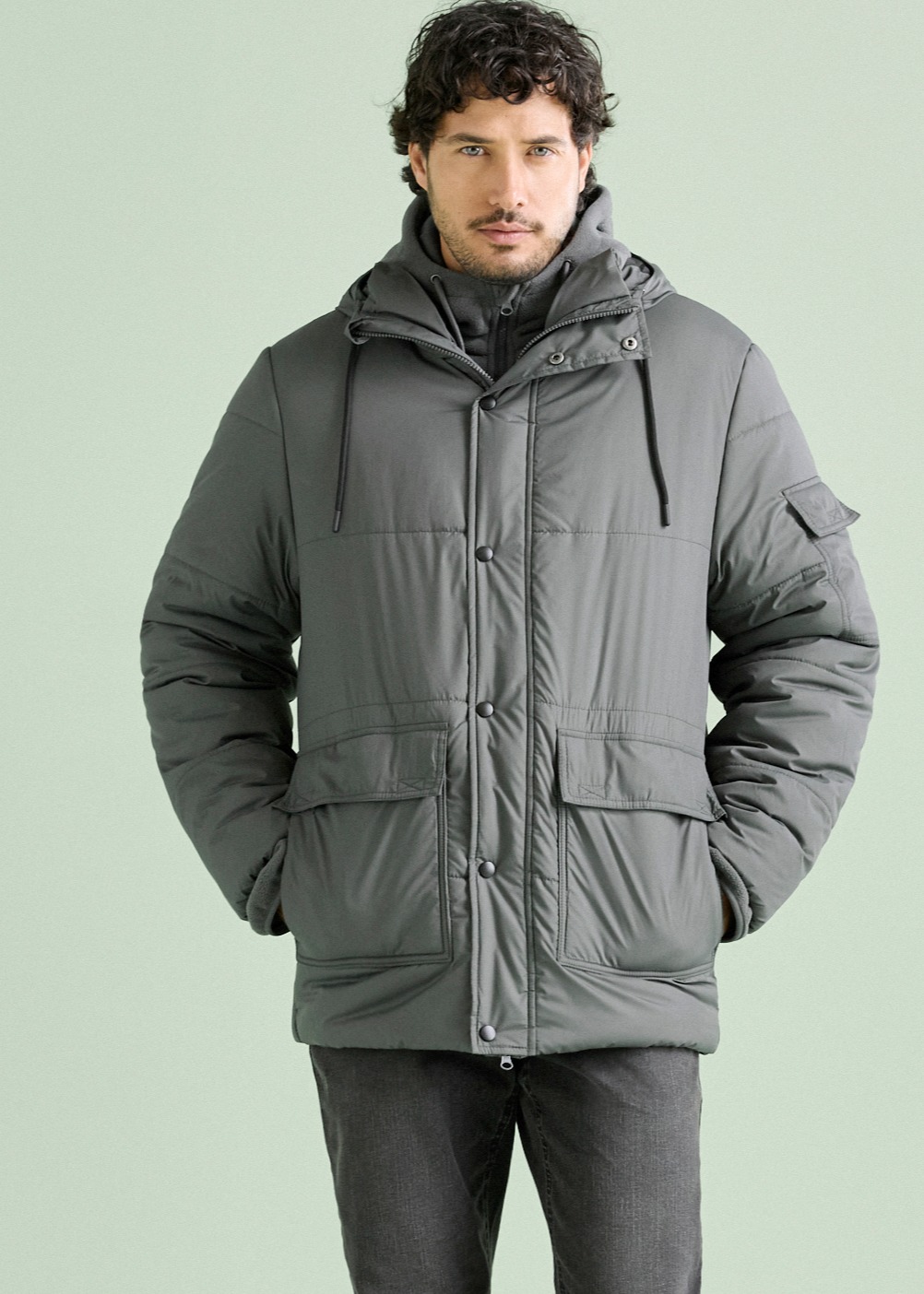 Ein Mann trägt eine stilvolle, graue Steppjacke mit Kapuze und praktischen Taschen.