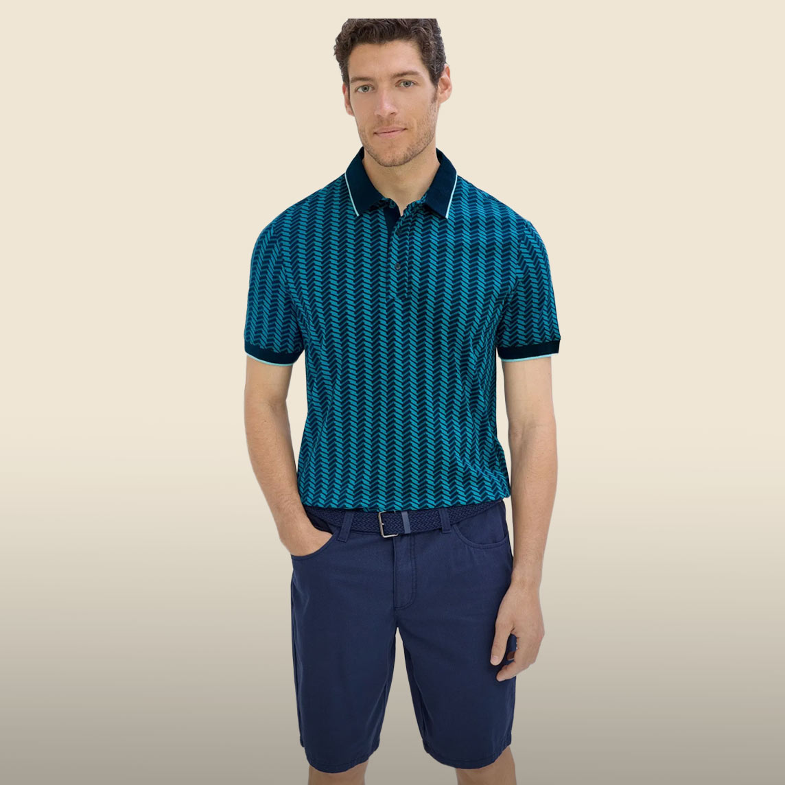 Gemustertes Polohemd in Blau-Türkis, kombiniert mit dunkelblauer Hose und Gürtel.