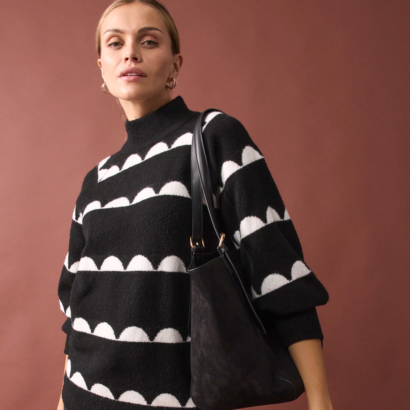 Schwarz-weißer Pullover kombiniert mit schwarzer Hose und schicker Handtasche.