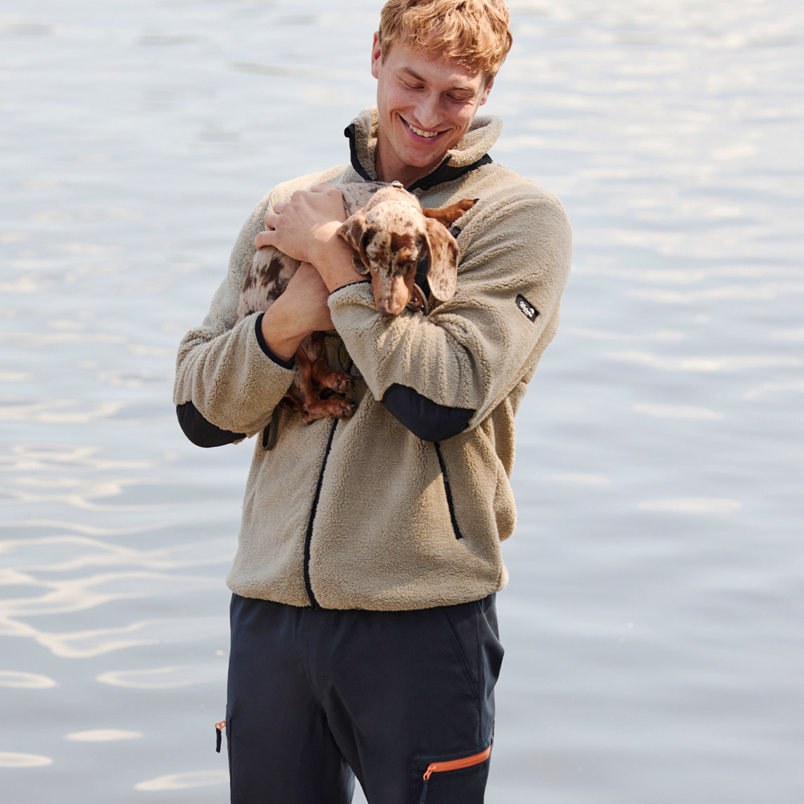 Beige Fleecejacke mit schwarzer Brusttasche, kombiniert mit dunkler Hose.