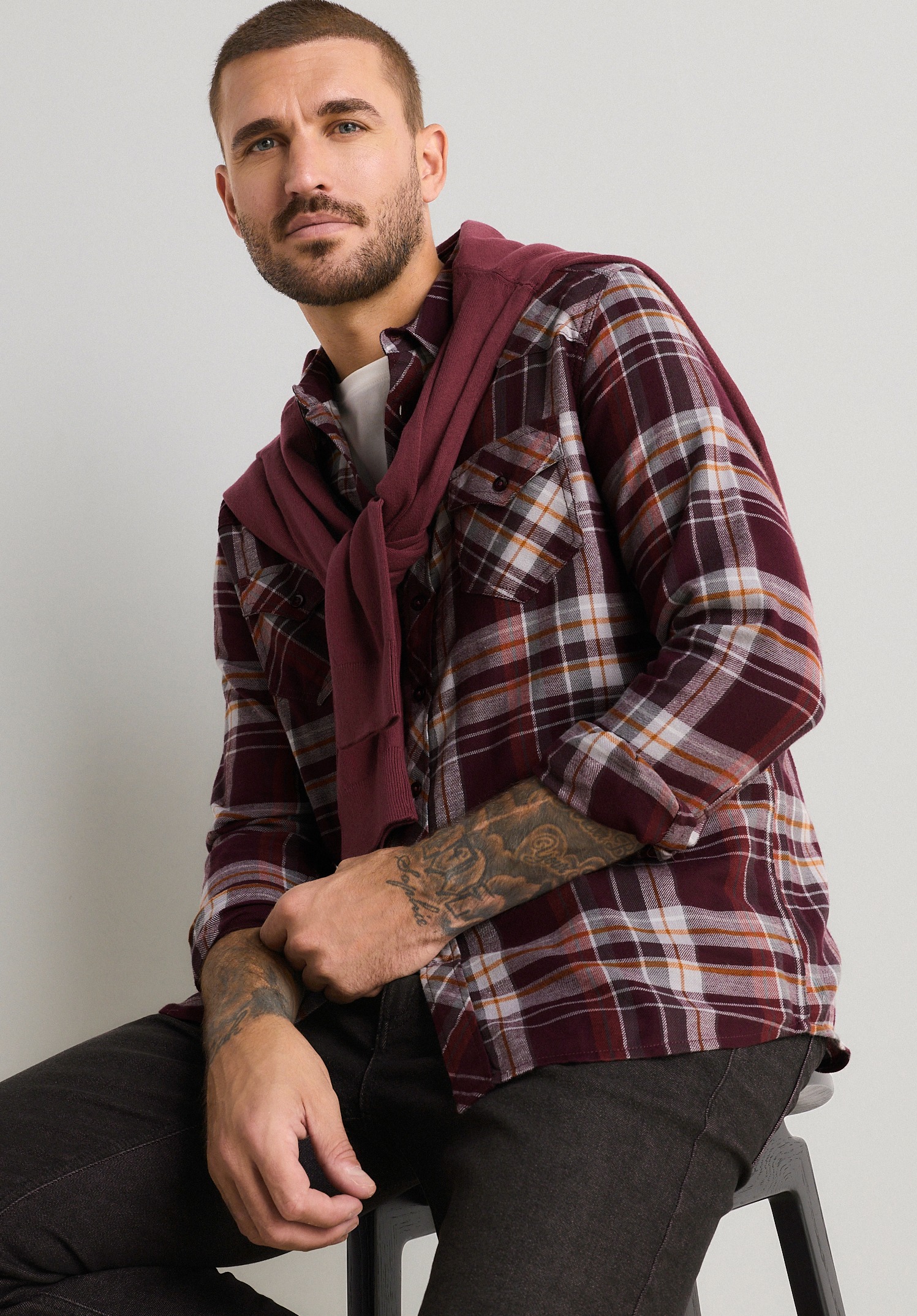 Kariertes Hemd in Bordeauxrot, dunkle Jeans und passender Pullover.