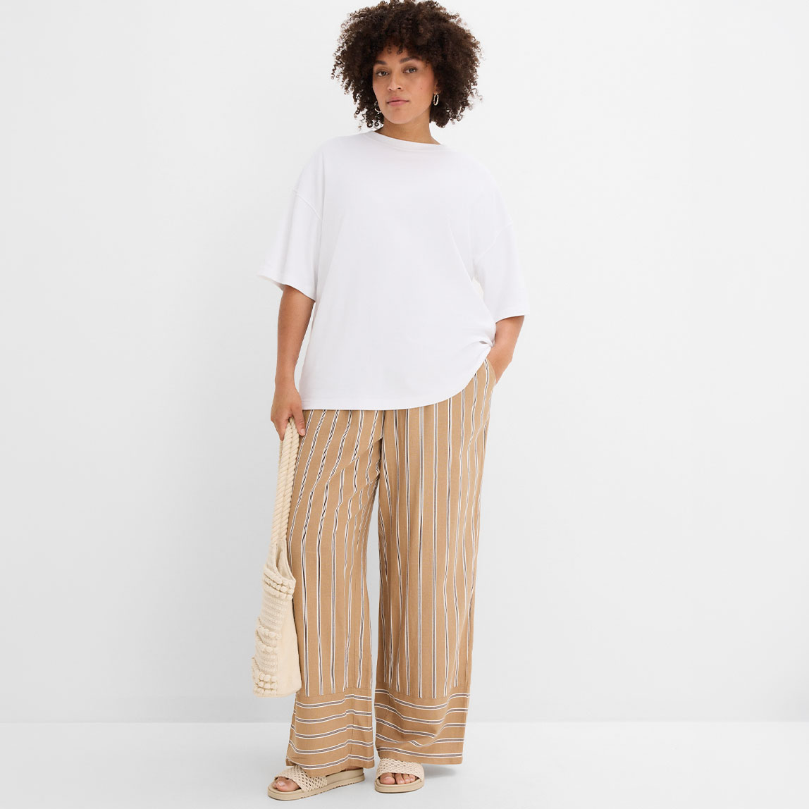 Weißes Oversize-Shirt, gestreifte weite Hose, dazu Sandalen.