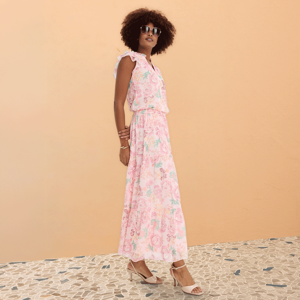 Luftiges Sommerkleid in Rosa mit Blumenmuster, ärmellos und bodenlang. Goldene Sandalen vervollständigen den Look.