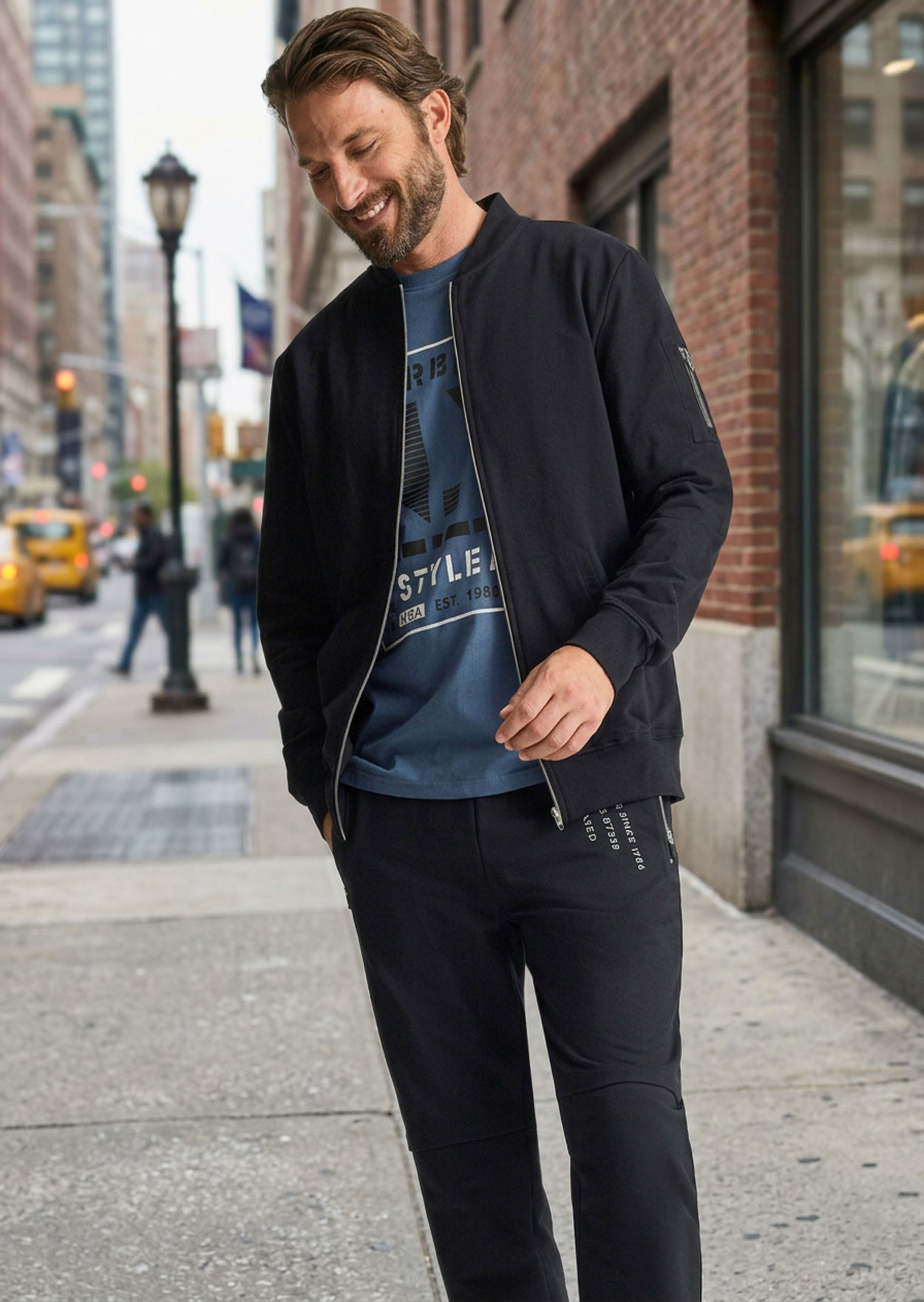 Schwarze Bomberjacke, blaues Shirt, dunkle Hose und weiße Sneaker.
