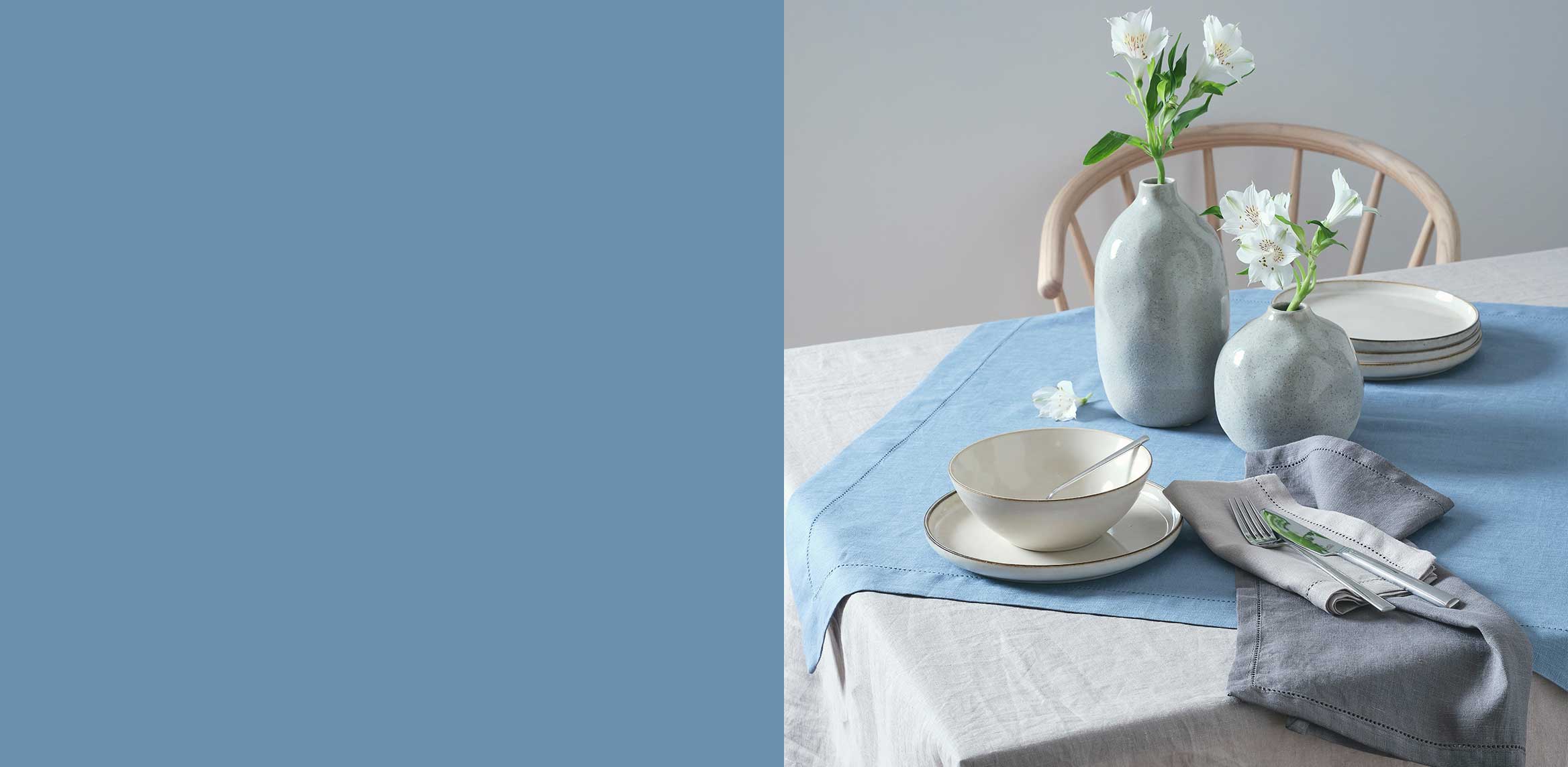 Elegantes Geschirr in sanften Pastelltönen auf hellblauem Tischtuch. Weiße Blumen als dezente Dekoration.