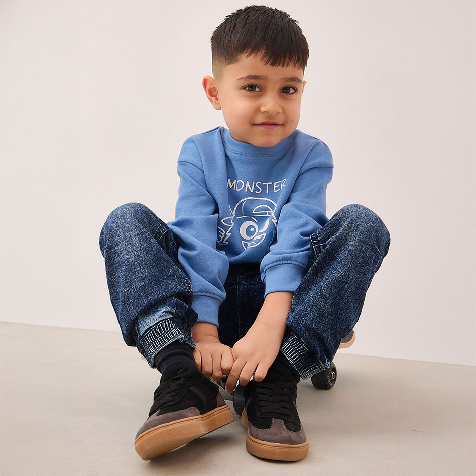 Blauer Pullover mit Monstermotiv, dunkle Jeans und schwarze Sneakers.