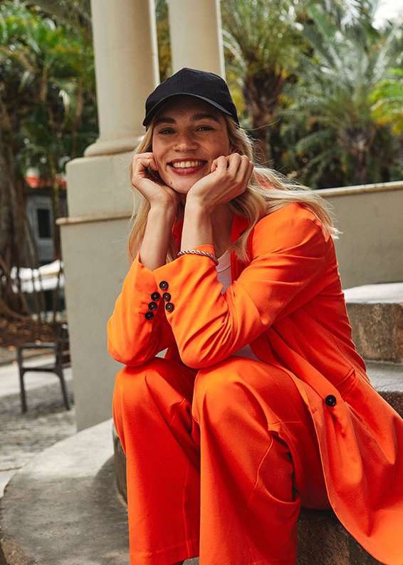 Leuchtend orangefarbener Anzug mit weiten Ärmeln, kombiniert mit einer schwarzen Baseballkappe.