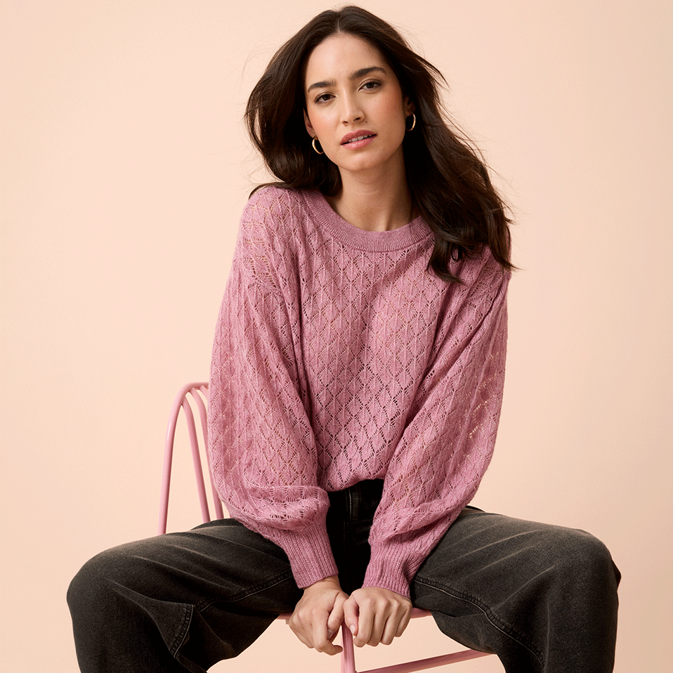 Weicher rosa Strickpullover mit Zopfmuster, kombiniert mit einer dunklen, weiten Jeans.