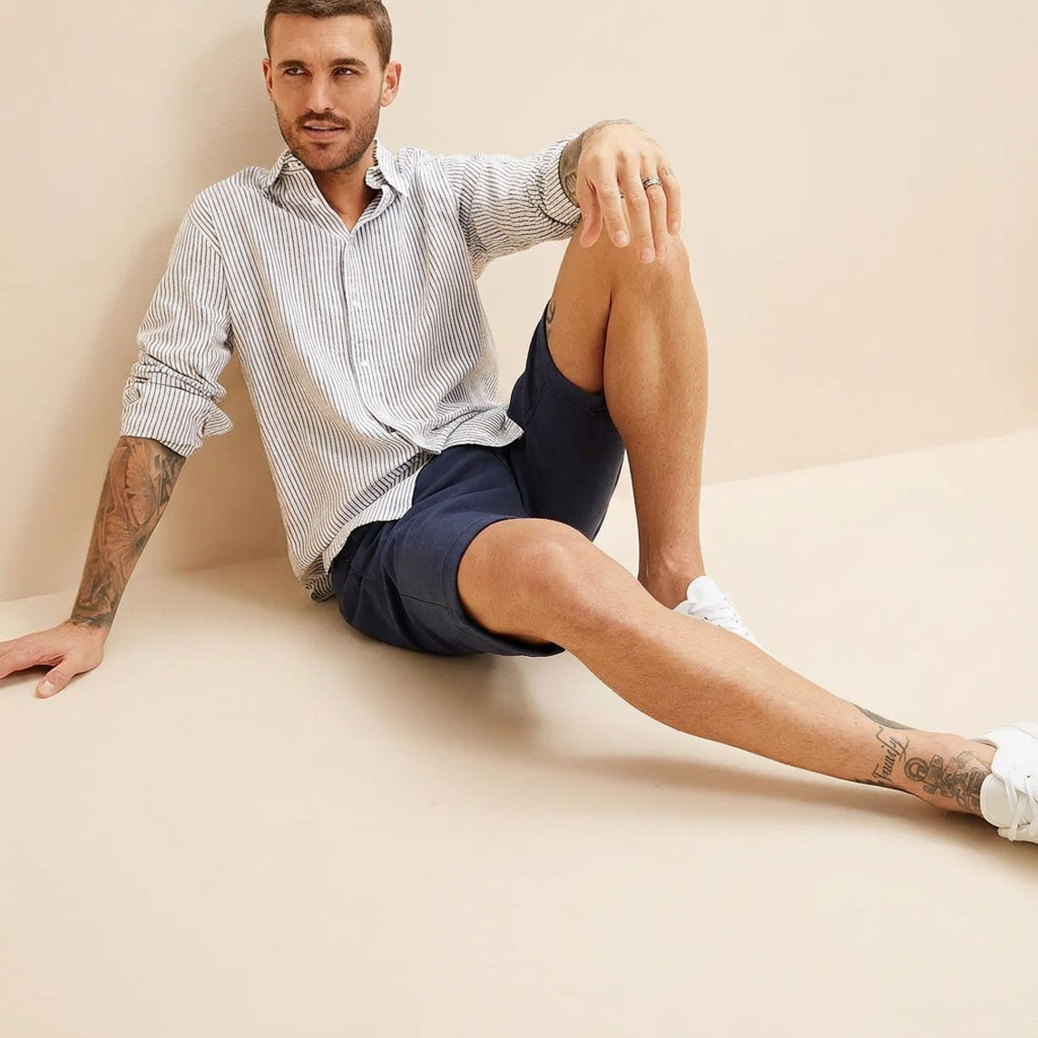Er trägt ein gestreiftes Hemd, dunkelblaue Shorts und weiße Sneaker.
