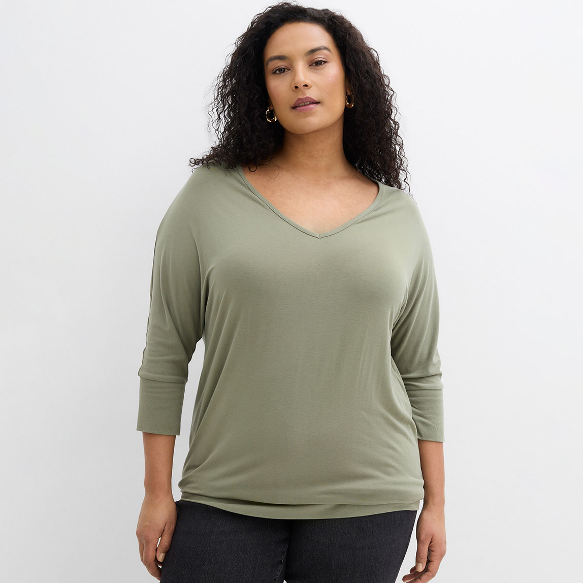 Entspannter Look mit salbeigrünem V-Ausschnitt-Shirt und dunkler Jeans.