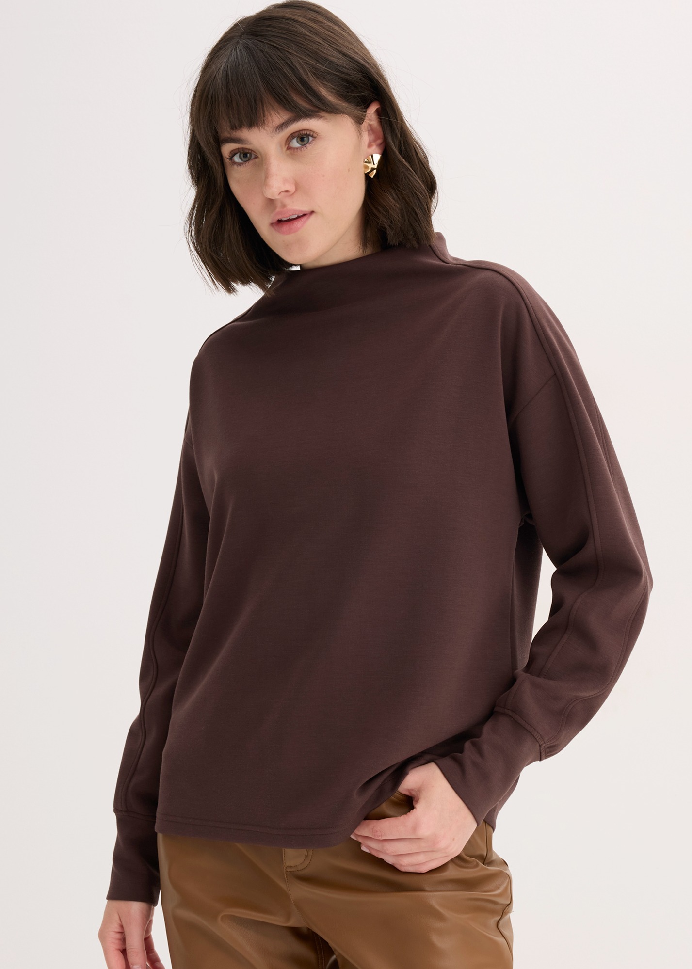 Sie trägt ein braunes Oversize Sweatshirt und eine braune Hose.