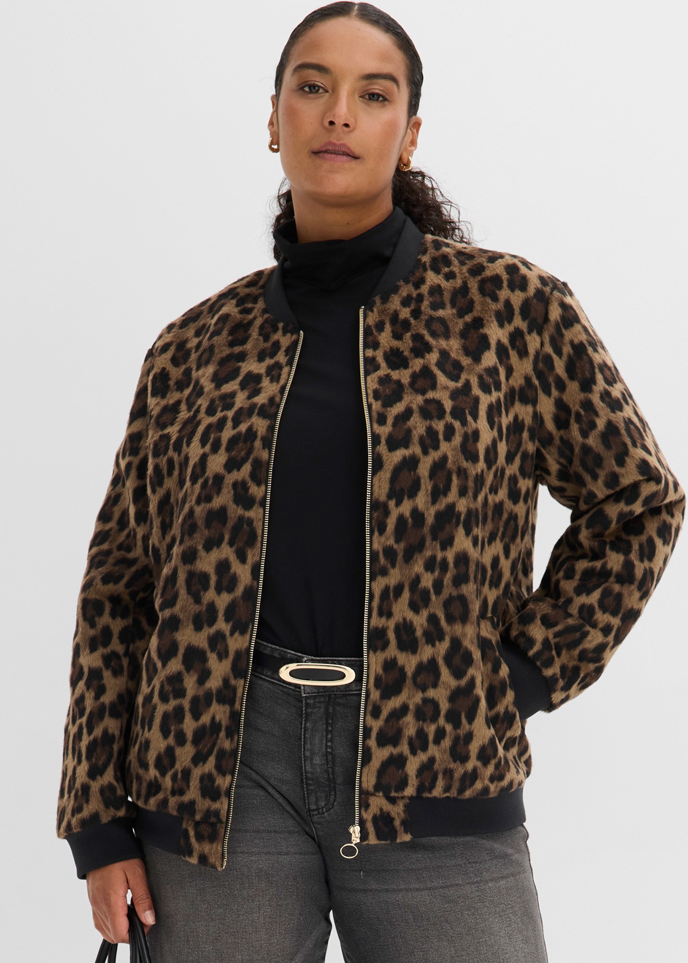 Leopard-Bomberjacke über schwarzem Rolli, kombiniert mit grauen Jeans und elegantem Gürtel.