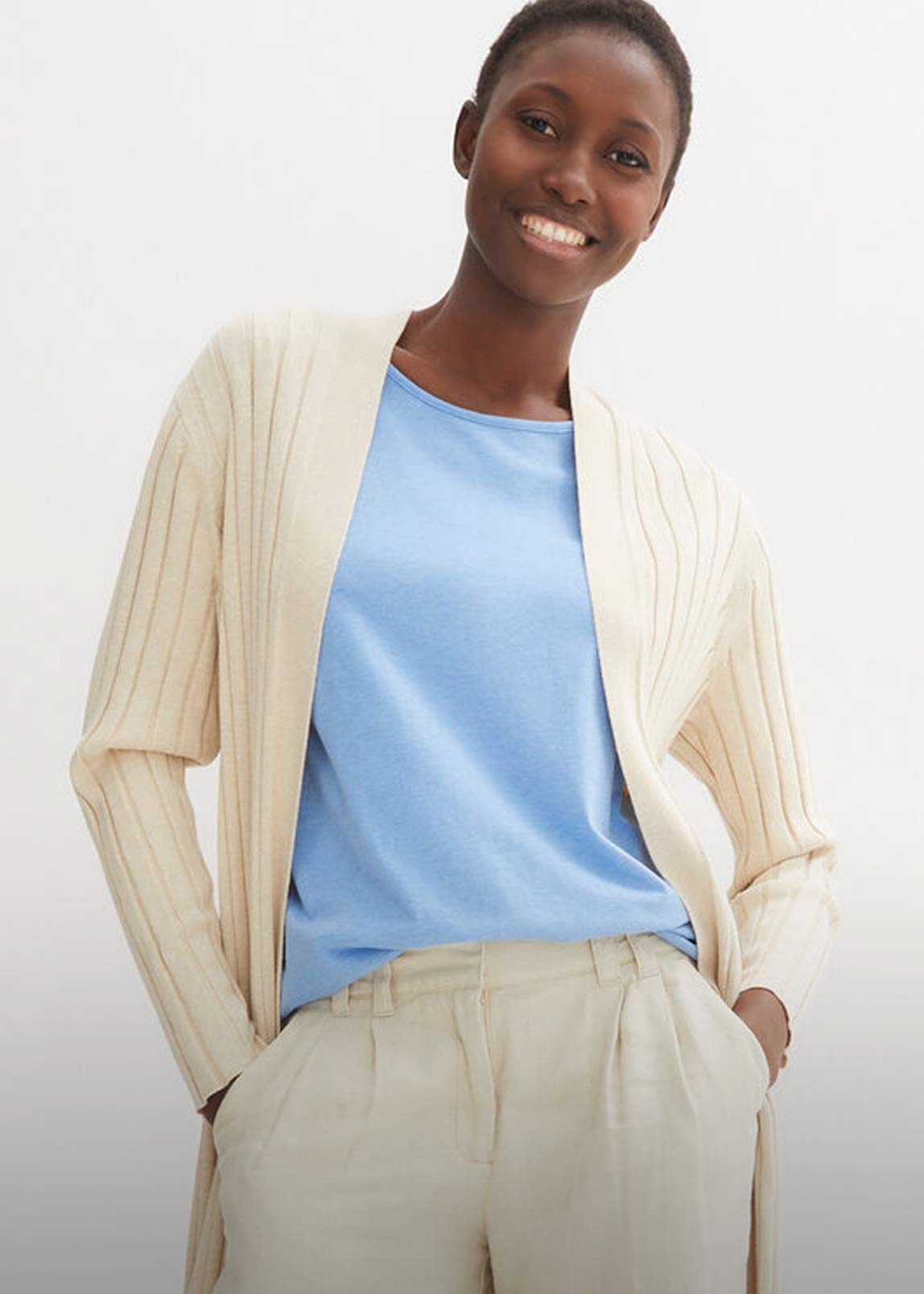 Cremefarbene Strickjacke über hellblauem Shirt, kombiniert mit heller Anzughose.