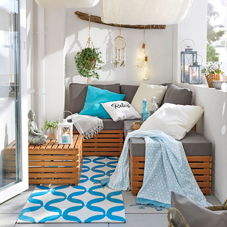 Gemütliche Balkon-Lounge mit weichen Decken, bunten Kissen und einem stylischen türkisfarbenen Teppich.
