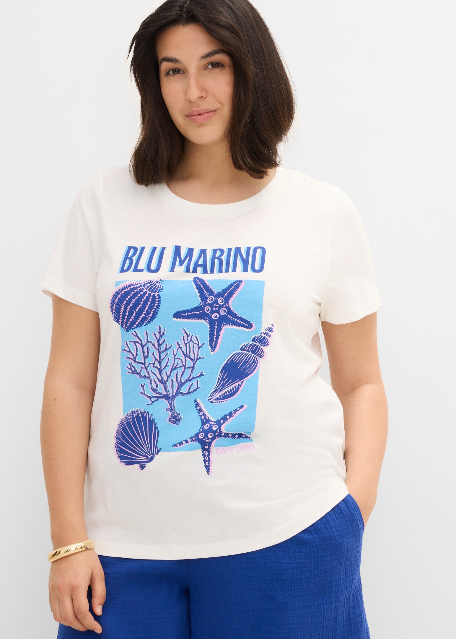 Weißes T-Shirt mit Muschel-Print, blaue Hose.